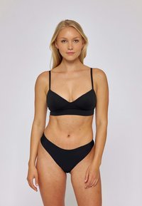 Czarny zestaw bikini, który składa się z trójkątnego biustonosza na cienkich, regulowanych ramiączkach oraz dopasowanych, niskich majtek. Gładka matowa tekstura, minimalistyczny design.