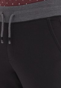 Zwarte trainingsbroek met een grijze geribbelde tailleband en trekkoord, voorzien van zijzakken en een gladde textuur.