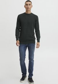 Pullover tricotat ribbed de culoare verde închis, cu sleeve raglan, asortat cu blugi slim-fit albaștri și adidași negri. Design simplu și casual.