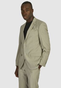 Lichtgrijze blazer met notch-lapels, twee knopen en zijzakken, gecombineerd met bijpassende broek en een zwart shirt eronder.