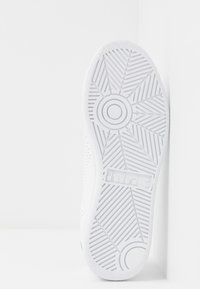 Suola di sneaker bianca con un motivo a battistrada geometrico, superficie liscia e logo sul lato. Il design è minimalista e elegante.