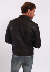 Brun läderjacka med en figurnära design, med hög krage och slät yta. Baket visar sömdetaljer och en ren silhuett.