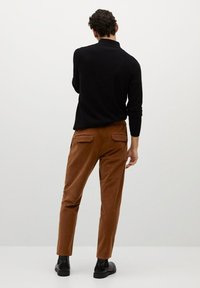 Czarna koszula z długim rękawem połączona z brązowymi sztruksowymi spodniami z dwoma tylnymi kieszeniami. Strój uzupełniają czarne buty.