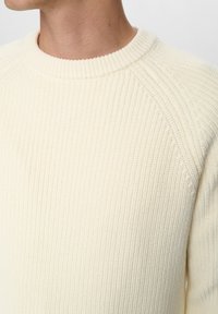 Lysebeige striktrøje med ribbet tekstur, rund halsudskæring og raglanærmer, der udstråler et blødt og hyggeligt udseende.