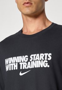 T-shirt in cotone nero con testo bianco in grassetto: "VINCERE INIZIA CON L'ALLENAMENTO" e un piccolo logo Nike. Collo a giro classico.
