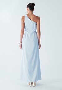 Světlomodré maxi šaty na jedno rameno s podšitým pasem, hladkou texturou a jemným splýváním, zdobené sponou na rameni.