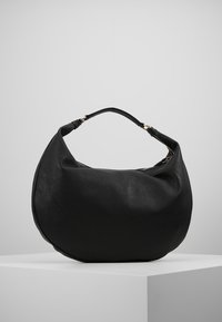 Czarna skórzana torebka w kształcie półksiężyca z jednym uchwytem i zamknięciem na zamek, eksponowana na białym pedestale na tle jasnoszarym.