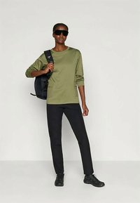 Tamnozelena košulja dugih rukava i crne hlače, uparene s crnim ruksakom i sunčanim naočalama. Udoban materijal; opušten kroj; minimalistički dizajn.