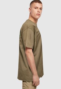 Oliven grøn bomulds t-shirt med løs pasform, rund udskæring og korte ærmer. Har et multicolort grafik på ryggen.