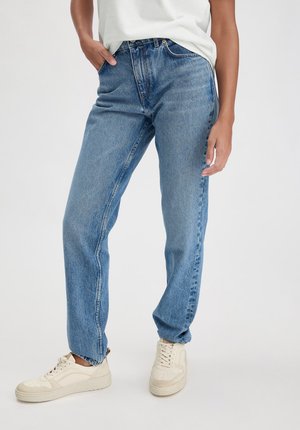 Blaue Jeans aus Denim mit entspannter Passform, hoher Taille, geraden Beinen und klassischem Fünf-Taschen-Design. Getragen mit beigen Sneakers.