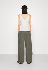 Light gray, sleeveless top with a V-neck and fitted hem, paired with loose, dark olive green trousers featuring front pockets and wide legs.