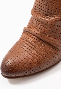 Botte en cuir tressé marron avec un bout pointu, présentant une finition texturée et deux bandes horizontales dans la zone de la cheville.