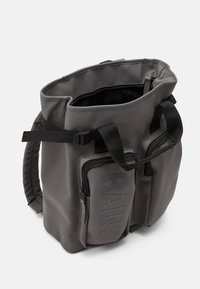 Mochila impermeable gris con aperturas dobles en la parte superior, correas ajustables y bolsillo frontal con cremallera que presenta un detalle en relieve de "RAINS".