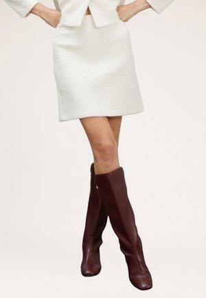Mini falda blanca de textura combinada con botas de cuero marrón hasta la rodilla, con un diseño ajustado y acabado suave.