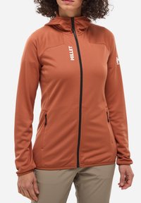 Hoodie léger à manches longues en orange brûlé, confectionné en tissu doux et texturé. Il comprend une fermeture éclair intégrale, deux poches latérales et des accents de logo.
