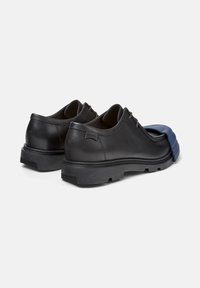 Zapatos de cuero negro con un detalle de goma azul en la punta, que muestran un diseño casual pero elegante. Las suelas son texturizadas para proporcionar agarre.