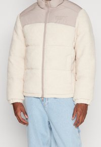 Krämfärgad fleecejacka med en slät beige axelpanel, dragkedja, och ribbade ärmslut, med en pösig design och sidofickor.