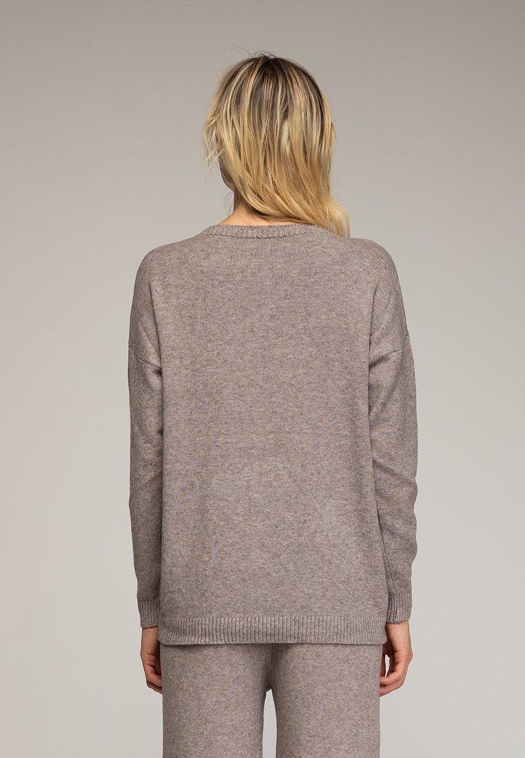 Suéter de punto beige con un corte relajado, dobladillo y puños acanalados, y un cuello redondo. La tela texturizada muestra sutiles variaciones en el tono.