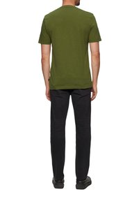 Olijfgroene t-shirt met korte mouwen, ronde hals en rechte zoom, gemaakt van zachte stof, gedragen met donkere jeans en zwarte schoenen.