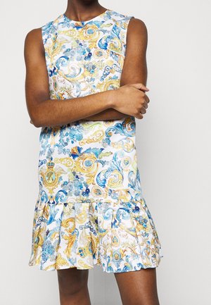 Biała sukienka bez rękawów z misternymi niebieskimi, złotymi i zielonymi kwiatowymi i barokowymi wzorami, z falbaną na dole, noszona przez osobę z założonymi skrzyżowanymi ramionami.