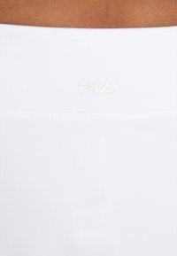 Vita atletiska shorts med en platt midja och präglad "FILA"-logga i ljusgrått. Slät yta utan synliga mönster eller detaljer.