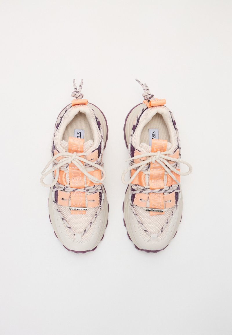 Sneaker con tomaia in mesh beige, accenti arancioni e suola in gomma viola. Presenta un sistema di lacci unico e un marchio sulla linguetta.