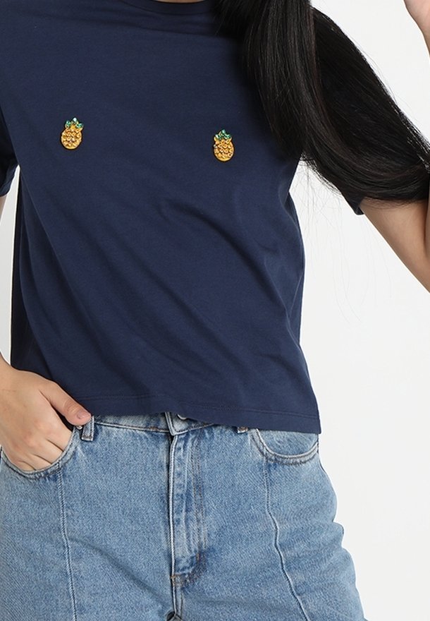 T-shirt a maniche corte blu navy con due design di ananas ricamati sul petto. Il tessuto è liscio e la vestibilità è rilassata.
