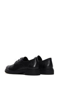 Chaussures en cuir noir au cuir lisse, à bout rond, à talon bas et à lacets. Accentuées par des coutures discrètes le long de la semelle.