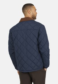 Marineblauwe gewatteerde jas met een bruine corduroy kraag, met een klassiek ontwerp, een gladde textuur en een ontspannen pasvorm.