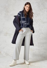 Pullover mit Marine-Muster und weißen Linien, kombiniert mit hellgrauen weiten Sweatpants und weißen High-Top-Sneakern; schwarze Daunenjacke.