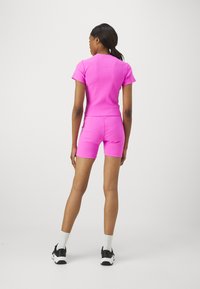 Tett, atletisk sett i lys rosa. Korte ermer topp med rund hals og matchende shorts. Materialet har en glatt og elastisk tekstur.