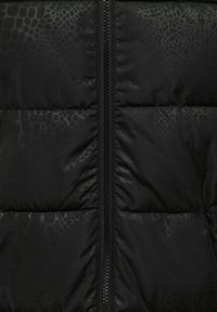 Black quilted jacket fabric with subtle reptile skin pattern and visible central zipper.