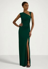 Πράσινο, εφαρμοστό φόρεμα με έναν ώμο και ραφές. Διαθέτει ψηλή σχισμή, πλαϊκή κοπή και λείο υλικό. Ανοιχτά τακούνια.