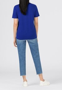 Blå bomullströja med kort ärm, kombinerad med ljusblå denimjeans och vita sneakers. Enkelt mönster, inga motiv eller synlig hårdvara.