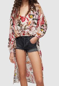 Halenka s květinovým vzorem, volného střihu z lehkého materiálu, s dlouhými rukávy a detailem na zavázání, v kombinaci s potrhanými džínovými šortkami.