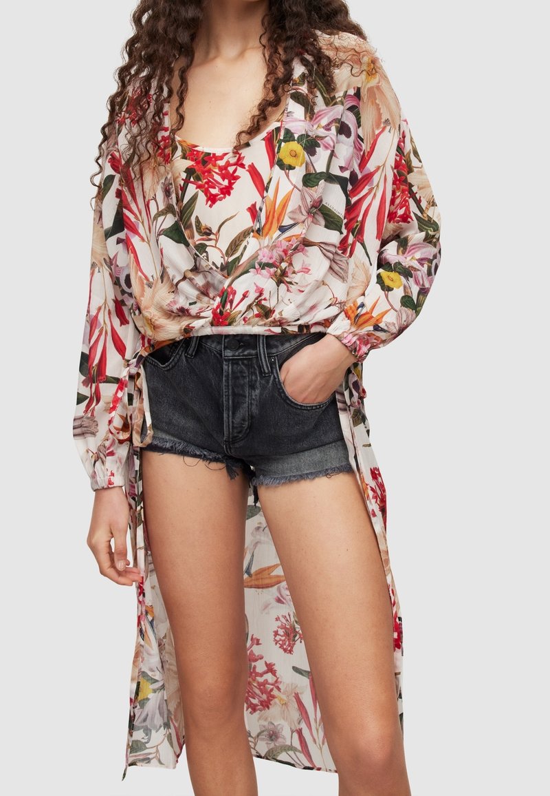 Halenka s květinovým vzorem, volného střihu z lehkého materiálu, s dlouhými rukávy a detailem na zavázání, v kombinaci s potrhanými džínovými šortkami.
