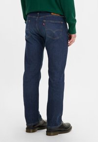 Dunkelblaue Denim-Jeans mit geradem Schnitt, ausgestattet mit charakteristischen Steppnähten an den hinteren Taschen, einem braunen Etikett am Bund und einer glatten Textur.