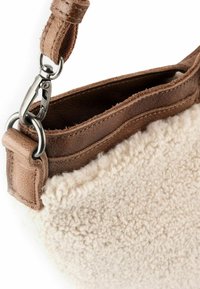 Lammfell-Handtasche mit beigem strukturiertem Außenmaterial, braunem Ledergriff und Metallelementen. Sie verfügt über eine plüschige, flauschige Textur an der Unterseite.