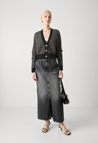 Μαύρος και κρεμ πλεκτός cardigan με κουμπιά, συνδυασμένος με μια σκούρα τζιν φούστα maxi με μπροστινό σκίσιμο. Μαύρη τσάντα και παπούτσια ανοιχτής μύτης.