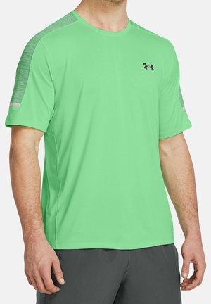Homme portant un t-shirt de sport vert vif à manches courtes avec des rayures à motifs sur les épaules et un pantalon gris foncé.