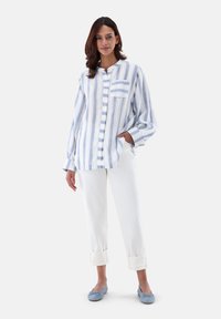 Camicia a righe blu e bianche con chiusura a bottoni, taschino sul petto e vestibilità rilassata, abbinata a pantaloni bianchi con risvolto e ballerine blu.