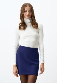 Weißes, geripptes Rollkragenoberteil, kombiniert mit einem enganliegenden, dunkelblauen Miniskirt. Das Outfit hat lange Ärmel und eine glatte Textur.