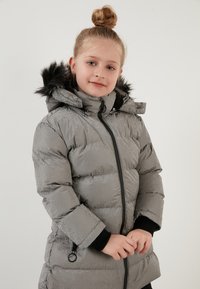 Sølv pufjakke med en skinnende finish, udstyret med hætte i sort kunstpels, lynlåslukning og ribbet mansjetter.