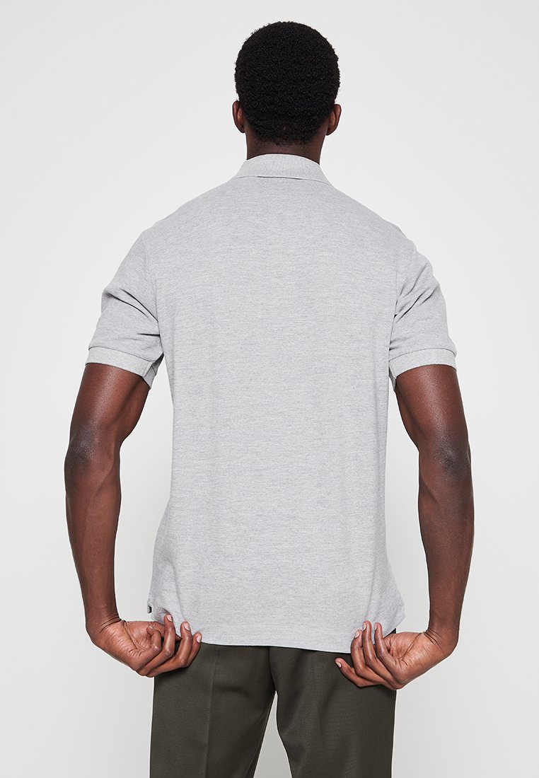 Grünes Poloshirt aus glattem Stoff, mit Kragen und kurzen Ärmeln. Der Rücken hat ein dezentes Saumdetail.