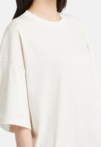 Överdimensionerad vit bomull t-shirt med rundad halsringning och korta ärmar. Har en liten broderad logotyp på bröstet. Slät textur.