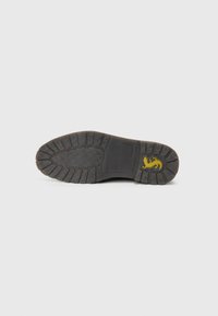 Suola di una scarpa nera con battistrada decorato, marchio di taglia 41 e logo giallo vicino al tallone su uno sfondo chiaro e semplice.