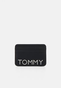 Černý kožený držák na karty s několika přihrádkami na karty; na přední straně najdete stříbrné logo "TOMMY". Hladká textura a elegantní design.