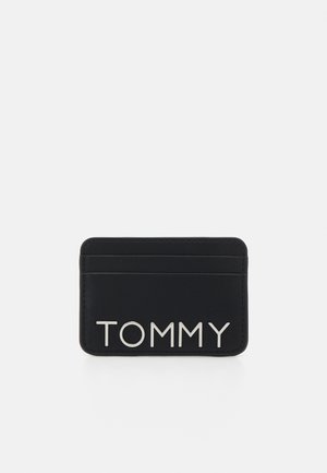 Tarjetero de cuero negro con múltiples ranuras para tarjetas; presenta un logo plateado "TOMMY" en la parte frontal. Textura suave y diseño aerodinámico.
