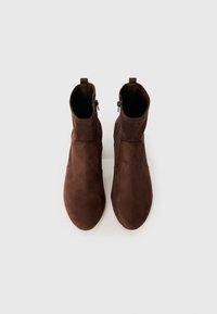 O pereche de ghete maro din suede, cu fermoare pe lateral, văzută dintr-o parte, pe un fundal alb simplu.