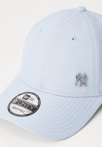 Svjetloplavi bejzbol kapa od tkanine s zakrivljenim vizorom. Ima srebrni logo New York Yankees i podesivu traku straga.